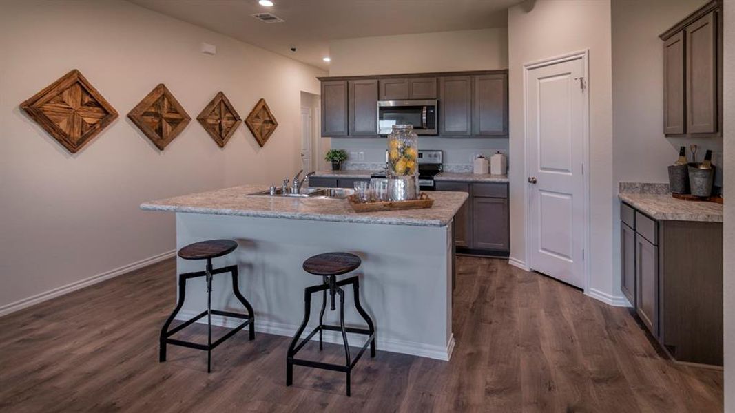 Kitchen featuring a central island with a built-in sink, stone-finish countertops, grey cabinetry, stainless steel appliances, and wood-finish flooring