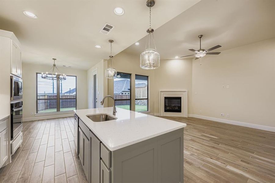 Kitchen featuring white cabinets, recessed lighting, decorative light fixtures, a glass covered fireplace, and light wood-style flooring