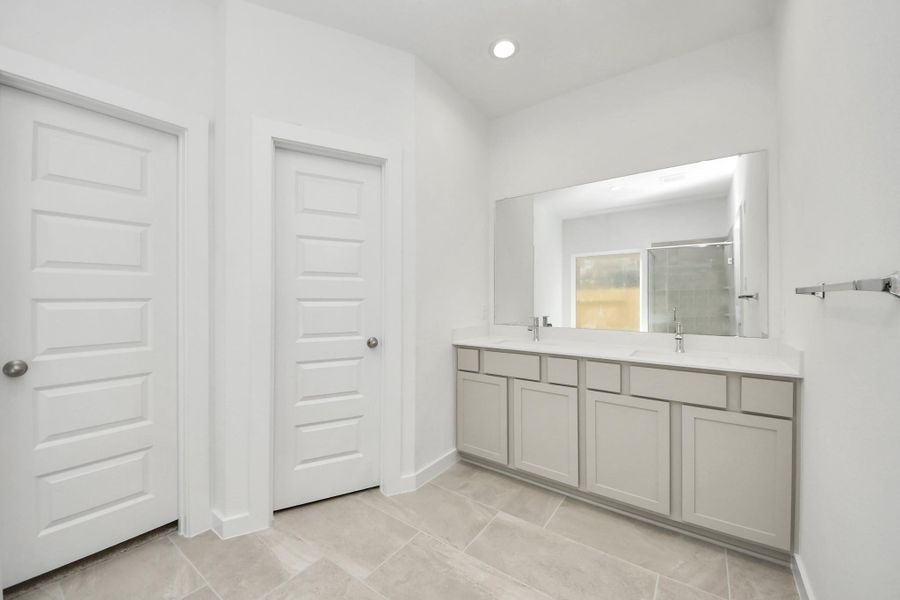 Escape to a spa-like oasis in this primary bathroom. Enjoy a walk-in shower with tile surround, a separate garden tub with custom detailing, and an elegant vanity featuring light countertops, modern hardware, and beautiful vanity lights. Experience luxury and relaxation in every detail. Sample photo of completed home with similar floor plan. Actual colors and selections may vary.
