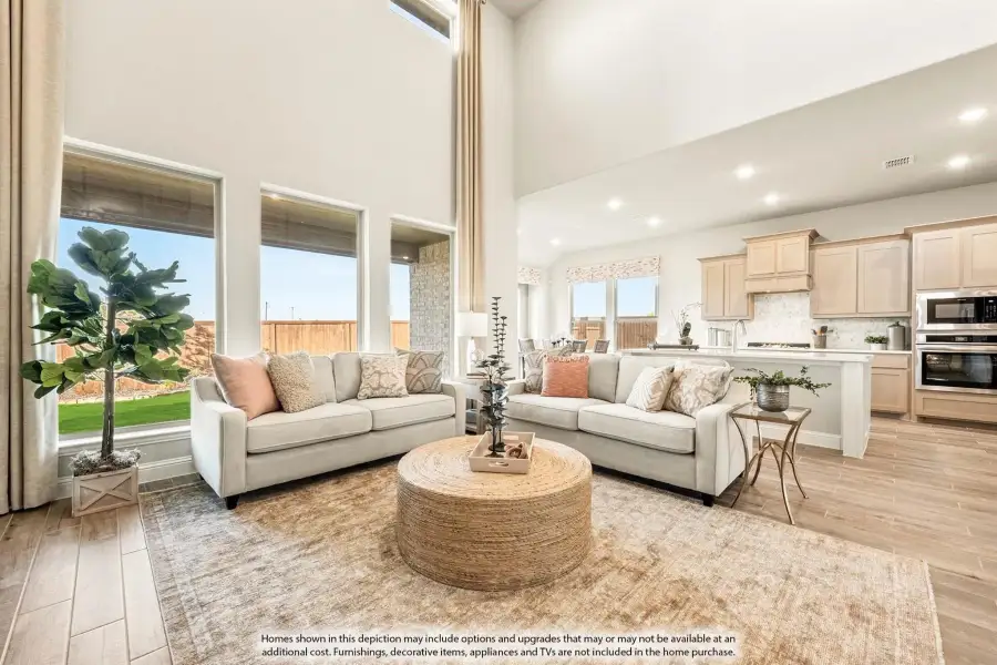 Open-concept living room with two-story ceiling, two sofas, and kitchen visible in background