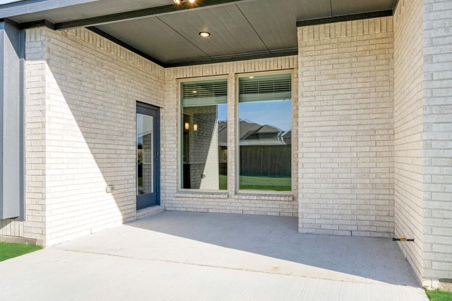 Covered back patio with concrete floor, light brick exterior, large window, and blue door with recessed ceiling light Covered back patio with concrete floor, light brick exterior, large window, and blue door with recessed ceiling light