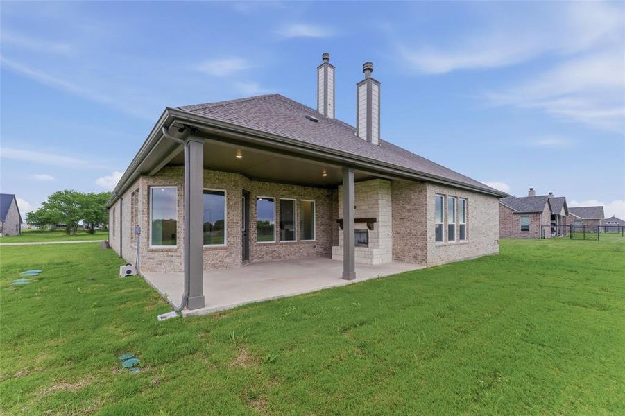 Rear exterior featuring a covered patio, brick exterior, outdoor fireplace, multiple windows, and dual chimneys