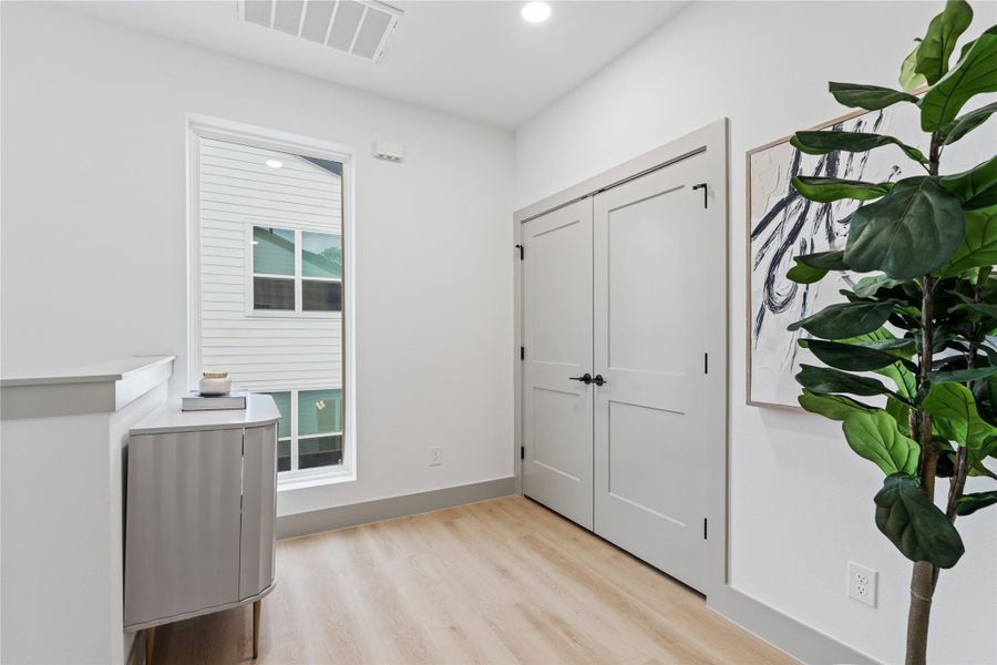 This bright and versatile landing makes a perfect transition space—ideal for a reading nook, gallery wall, or drop zone. Natural light floods in through a tall picture window, highlighting the warm-toned SPC flooring and clean architectural lines throughout.
