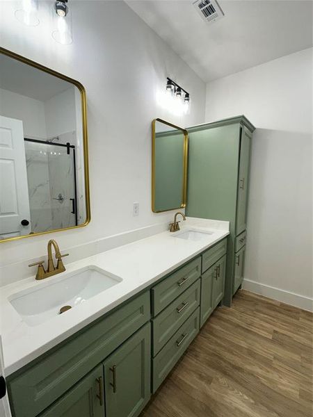 Bathroom featuring double vanity, dark wood-type flooring, and a marble finish shower