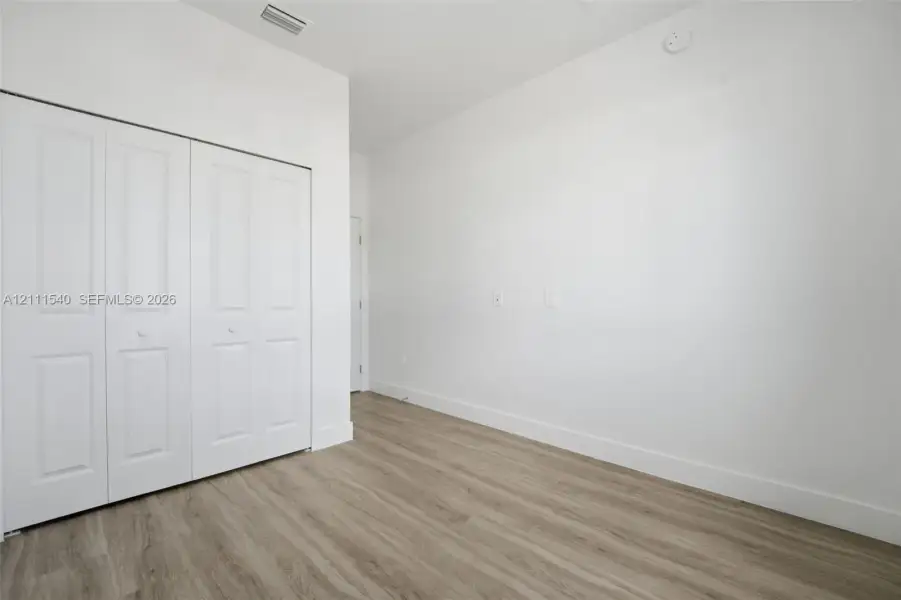 Room featuring wood-finish flooring, white walls, and a white bi-fold closet door