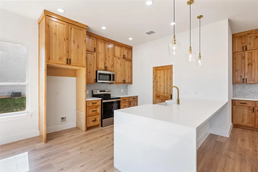 Kitchen with a peninsula, appliances with stainless steel finishes, pendant lighting, light stone countertops, and recessed lighting