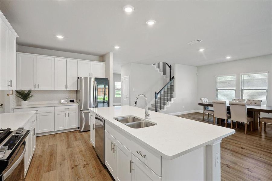 Kitchen with sink, white cabinetry, light wood-type flooring, and a kitchen island with sink