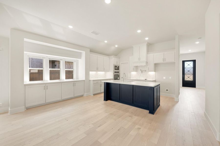 Open kitchen with white cabinets, navy blue island, light hardwood floors, and tile backsplash