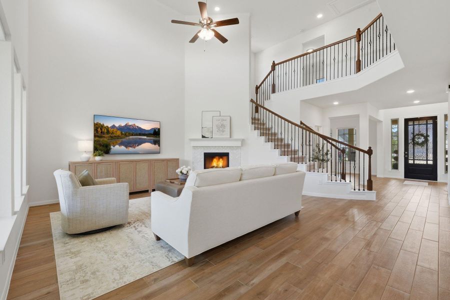 This spacious living room features high ceilings, a cozy fireplace, and a modern open staircase. Large windows provide ample natural light, while wood tile flooring adds warmth. The entryway is inviting, with a stylish front door and elegant finishes.