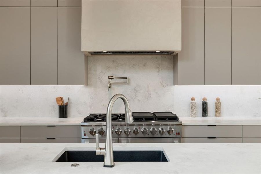 Modern kitchen featuring a stainless steel range with griddle, pot filler, and custom range hood