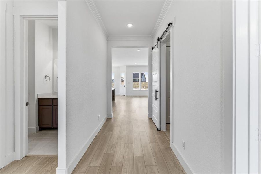 Hall with crown molding, a barn door, light wood-style flooring, and recessed lighting