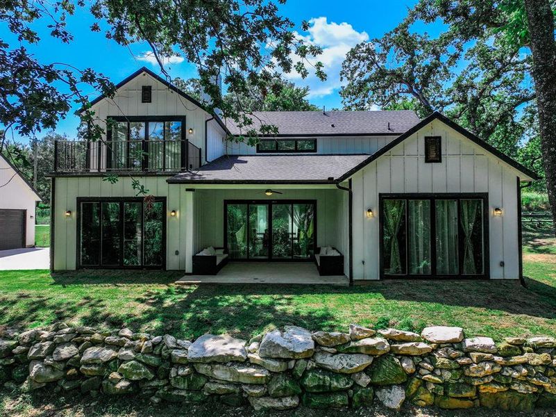 Rear view of house featuring a balcony, board and batten siding, a lawn, and roof with shingles Rear view of house featuring a balcony, board and batten siding, a lawn, and roof with shingles