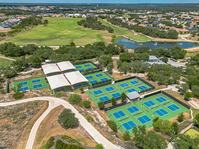 An aerial perspective reveals numerous tennis courts nestled amidst a verdant landscape with a golf course and a tranquil pond nearby. An aerial perspective reveals numerous tennis courts nestled amidst a verdant landscape with a golf course and a tranquil pond nearby.