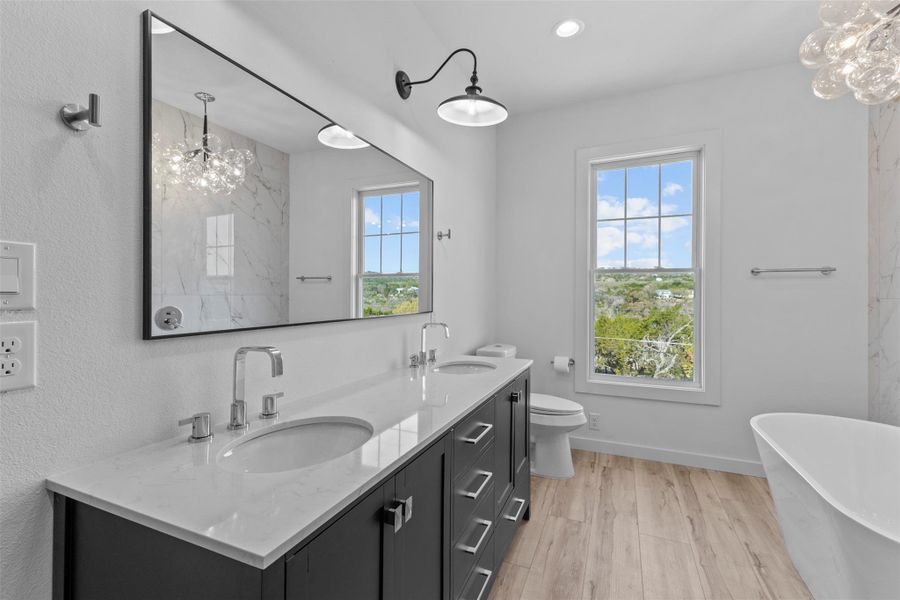 Bathroom featuring double vanity, a soaking tub, light wood finished floors, and a chandelier