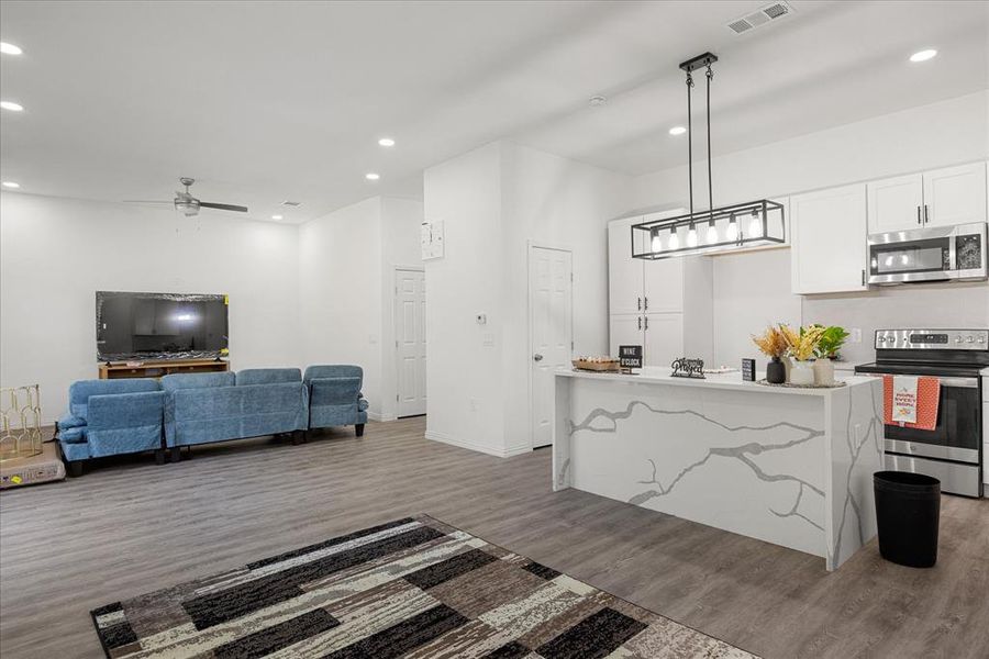 Kitchen featuring appliances with stainless steel finishes, white cabinetry, a kitchen island, dark hardwood / wood-style flooring, and decorative light fixtures