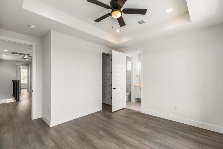 Primary bedroom with tray ceiling, ceiling fan, and private access to the en-suite bathroom. Primary bedroom with tray ceiling, ceiling fan, and private access to the en-suite bathroom.