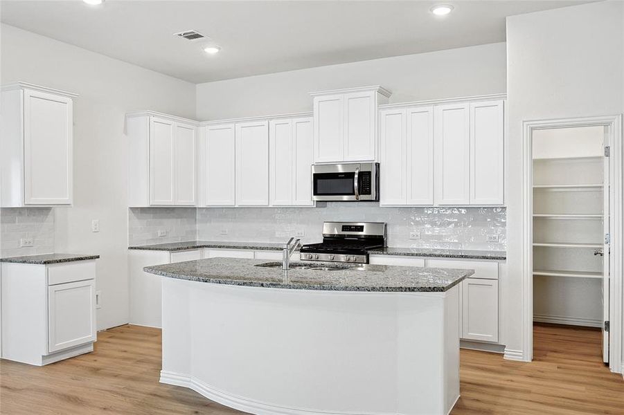 Kitchen with an island with sink, light hardwood / wood-style floors, white cabinets, and stainless steel appliances