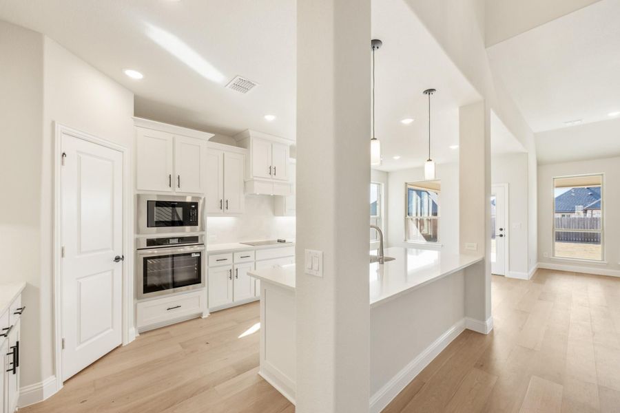 Open kitchen with white cabinets, stainless steel appliances, quartz island, and light hardwood floors