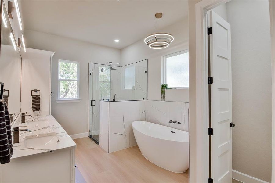 Bathroom featuring a soaking tub, a marble finish shower, light wood-style floors, double vanity, and recessed lighting Bathroom featuring a soaking tub, a marble finish shower, light wood-style floors, double vanity, and recessed lighting