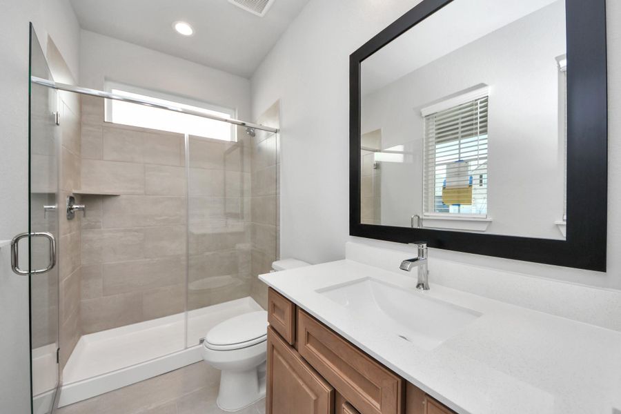 Secondary bath features tile flooring, walk-in shower tile surround, light stained wood cabinets, beautiful light countertop.