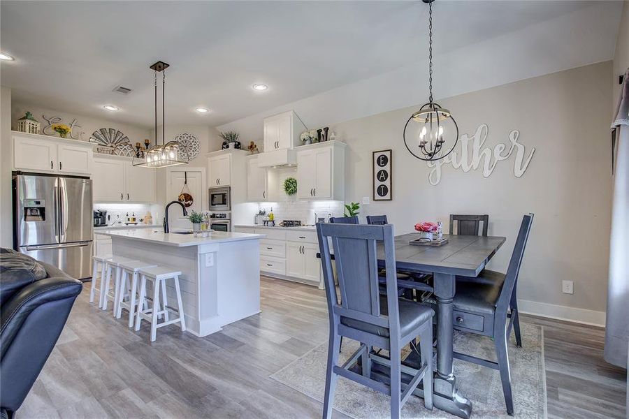 Kitchen with white cabinets, an island with sink, decorative light fixtures, and appliances with stainless steel finishes