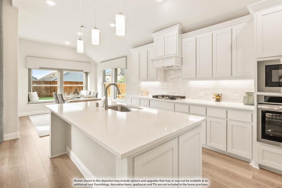 Kitchen with white cabinets, large center island with sink, pendant lights, and stainless steel appliances on light wood floors.