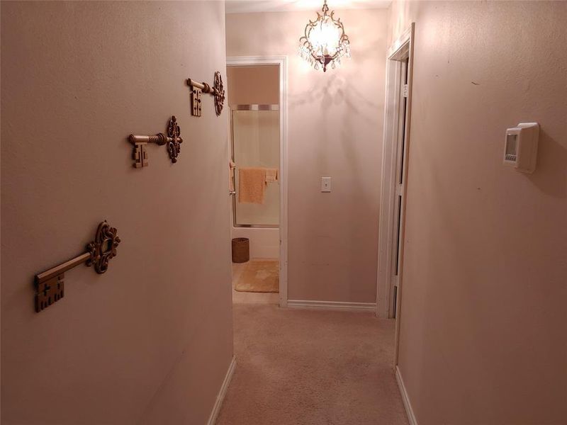 Hallway featuring a crystal chandelier, neutral-toned carpeting, and a visible interior doorway leading to a bathroom with a shower-tub combination