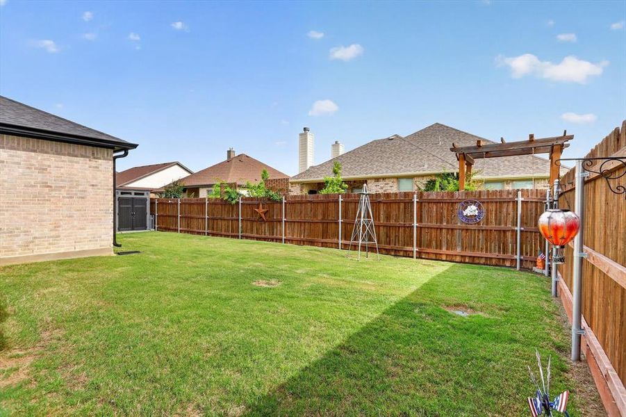 Expansive backyard featuring a lush lawn, privacy fencing, and a side-entry storage shed