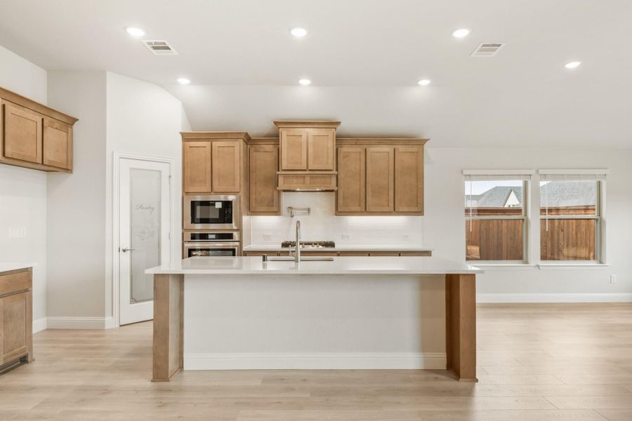 Kitchen with large center island, light wood cabinets, stainless steel appliances, and light hardwood floors Kitchen with large center island, light wood cabinets, stainless steel appliances, and light hardwood floors