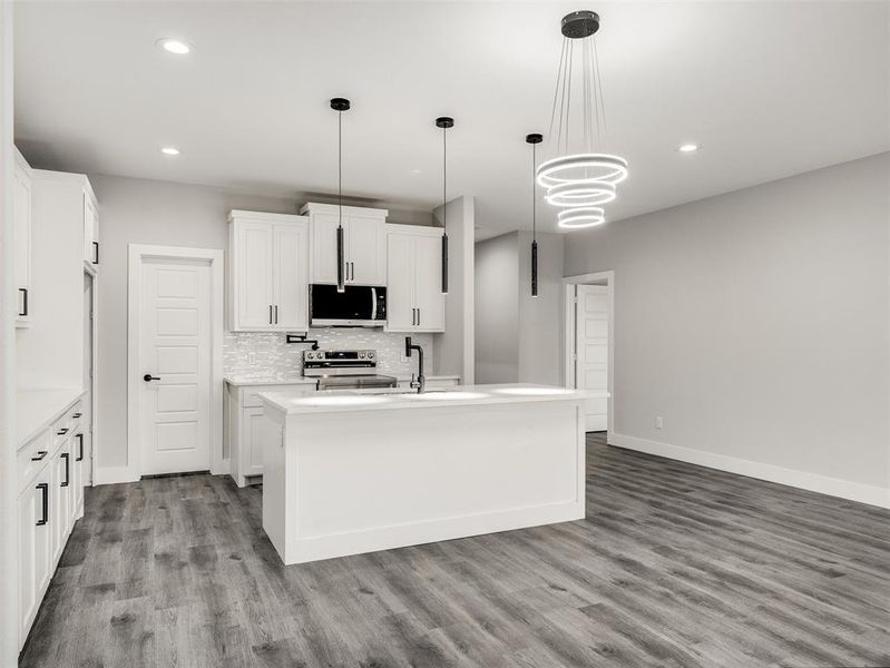 Kitchen featuring tasteful backsplash, stainless steel appliances, a kitchen island with sink, decorative light fixtures, and white cabinetry