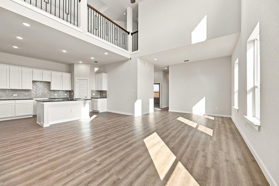 Open-concept living area with two-story ceiling, hardwood floors, and white kitchen with island and herringbone backsplash.
