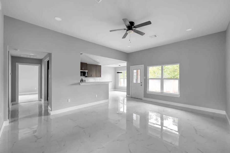 This modern home features an open floor plan with a spacious living area, sleek marble flooring, and ample natural light. The kitchen is partially separated by a breakfast bar, and there's a ceiling fan for added comfort. The neutral gray walls provide a contemporary touch.