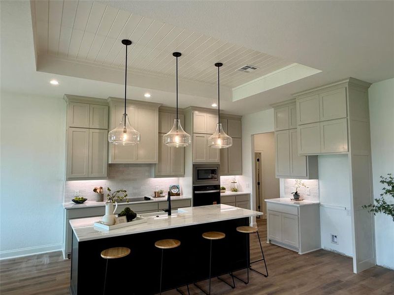 Expansive kitchen featuring a large central island with a contrasting base, white countertops, and three pendant lights