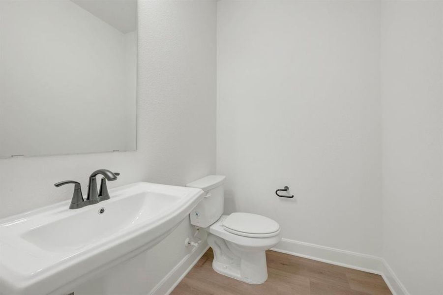 Powder room featuring a pedestal sink with dark bronze fixtures, a wall-mounted mirror, and wood-finish flooring