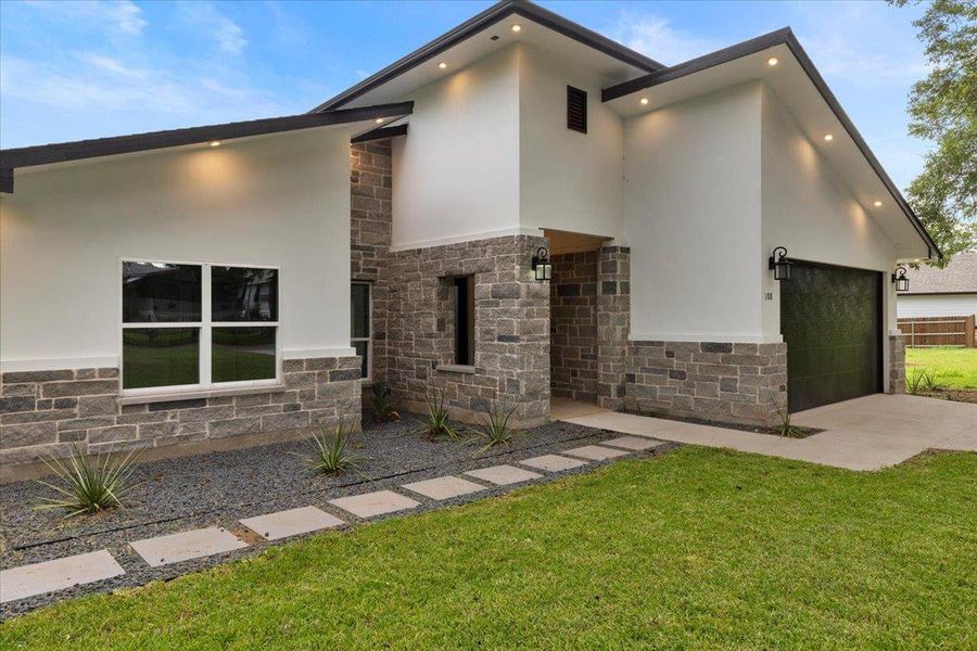 View of front of property featuring stone siding, stucco siding, concrete driveway, a front lawn, and a garage View of front of property featuring stone siding, stucco siding, concrete driveway, a front lawn, and a garage