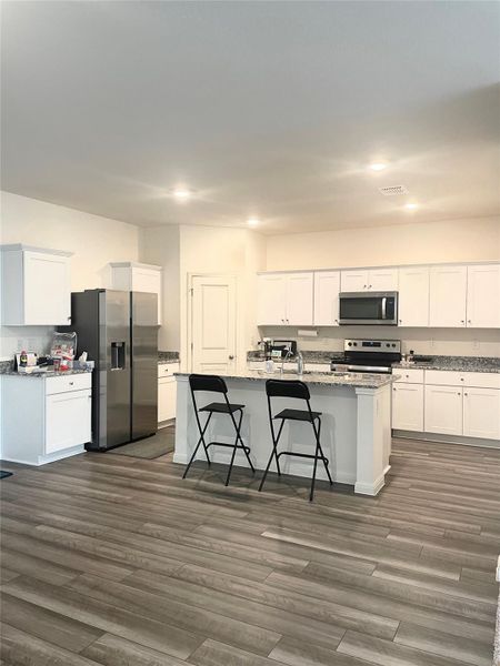 Kitchen featuring white cabinetry, stainless steel appliances, light stone countertops, dark wood-style floors, and recessed lighting