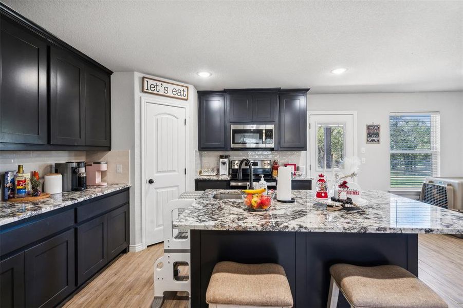 Kitchen featuring a kitchen bar, light stone countertops, tasteful backsplash, light hardwood / wood-style floors, and an island with sink