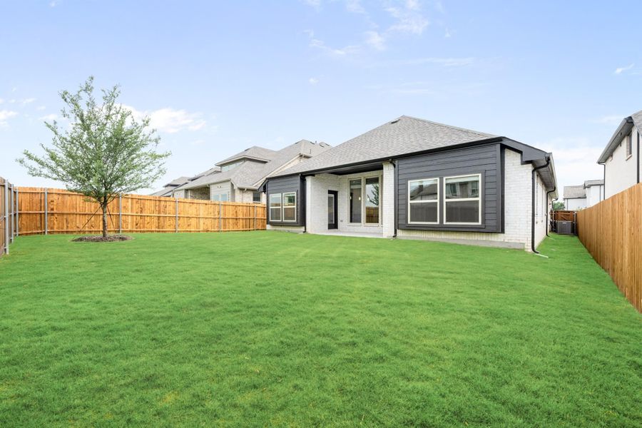 Backyard of single-story home with gray siding, brick exterior, large lawn, and wood privacy fence Backyard of single-story home with gray siding, brick exterior, large lawn, and wood privacy fence