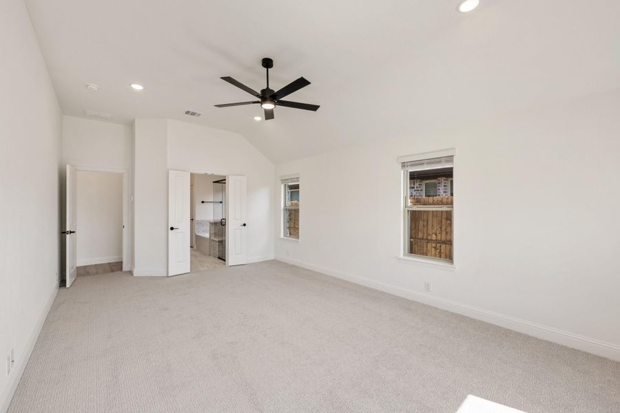 Spacious bedroom with vaulted ceiling, black ceiling fan, carpet flooring, and open door to ensuite bathroom. Spacious bedroom with vaulted ceiling, black ceiling fan, carpet flooring, and open door to ensuite bathroom.