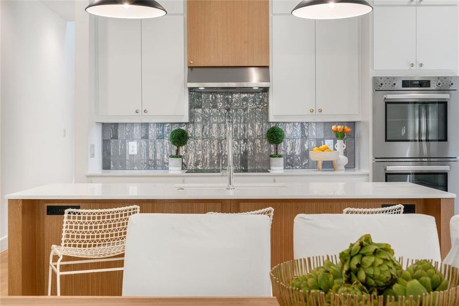 Kitchen featuring stainless steel double oven, backsplash, extractor fan, and white cabinetry