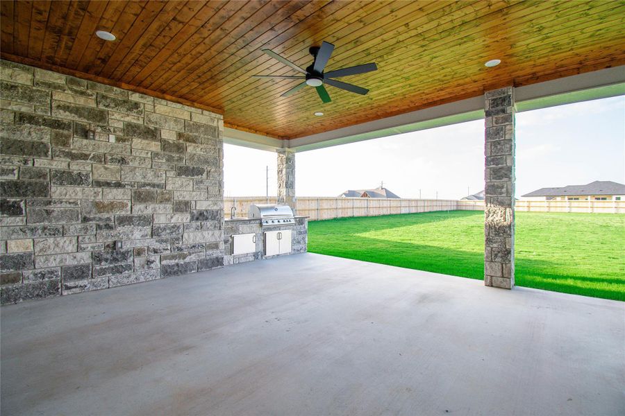 An inviting covered patio featuring an outdoor kitchen, perfect for entertaining guests with views of the vast yard.