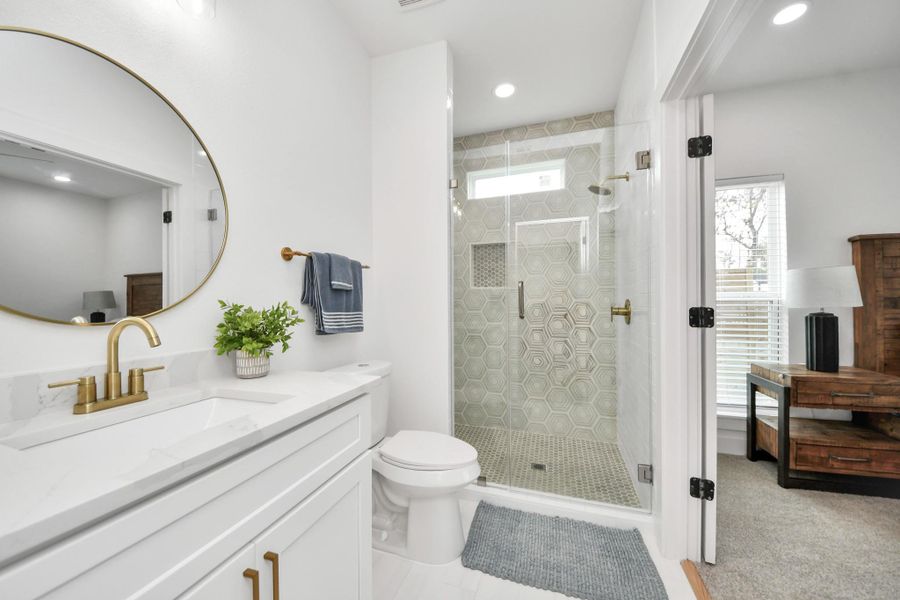 Elegant bathroom featuring a spacious glass-enclosed shower with stylish hexagonal tiles, complemented by a sleek vanity with a modern circular mirror and gold fixtures. Elegant bathroom featuring a spacious glass-enclosed shower with stylish hexagonal tiles, complemented by a sleek vanity with a modern circular mirror and gold fixtures.