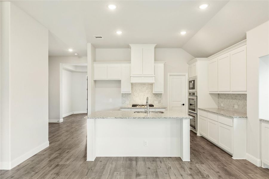 White kitchen with center island, granite countertops, stainless steel appliances, and wood-look floors