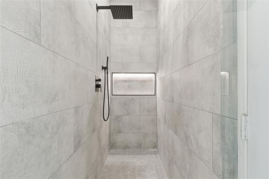 Walk-in shower with textured light gray tile walls and floor, featuring a built-in recessed niche with accent lighting Walk-in shower with textured light gray tile walls and floor, featuring a built-in recessed niche with accent lighting
