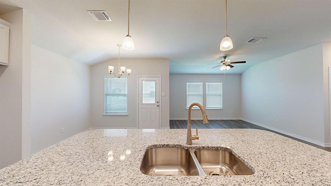 Kitchen featuring lofted ceiling, hanging lights, light stone counters, wood finished floors, and a ceiling fan