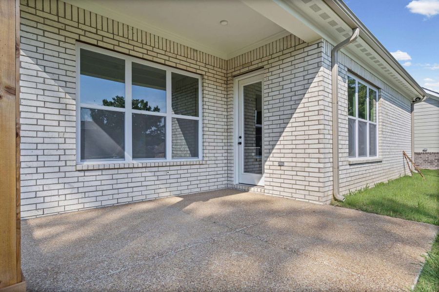 Covered patio featuring a concrete surface, white brick exterior, and multiple windows