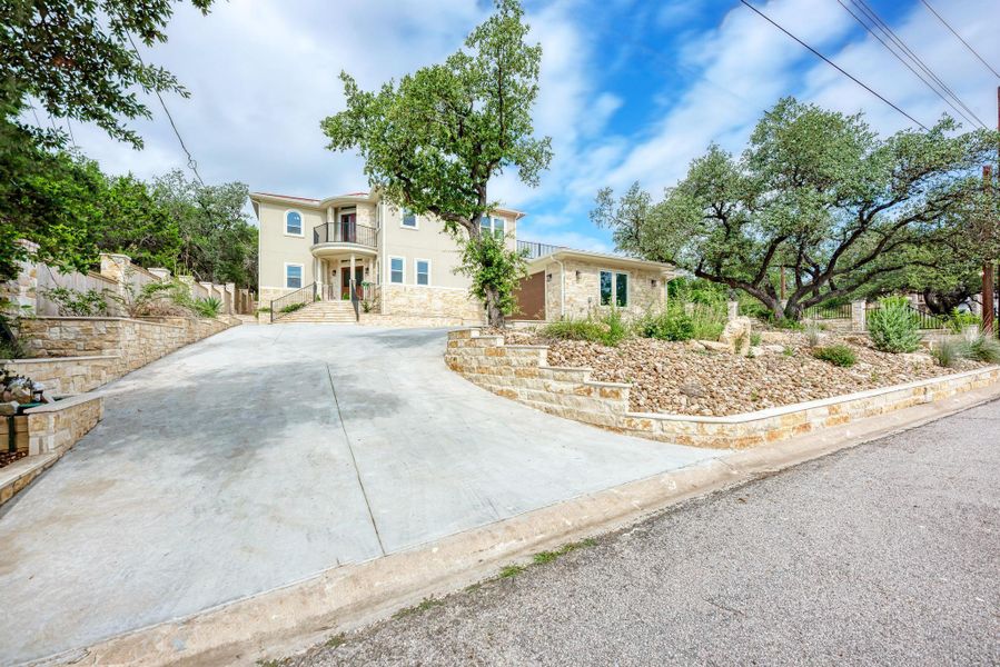 View of front of home featuring stone siding, concrete driveway, stucco siding, and a balcony