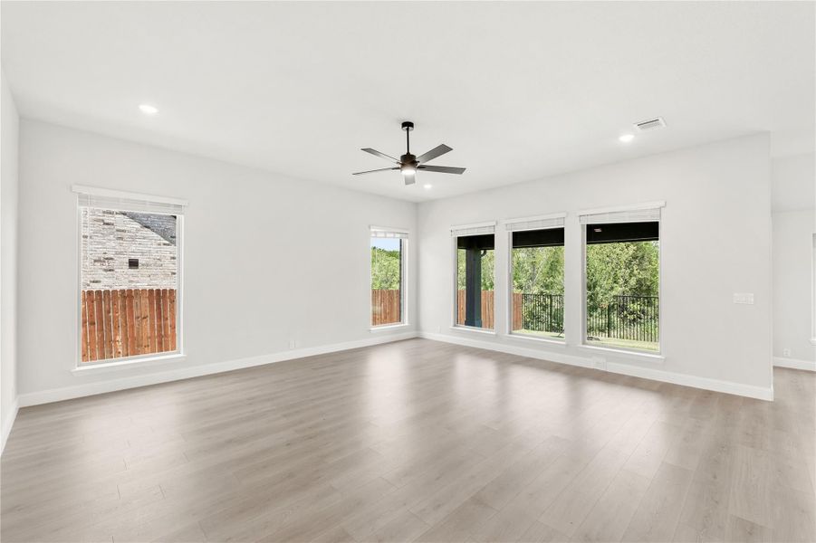 Empty living room with light wood floors, ceiling fan, and large windows overlooking a backyard Empty living room with light wood floors, ceiling fan, and large windows overlooking a backyard