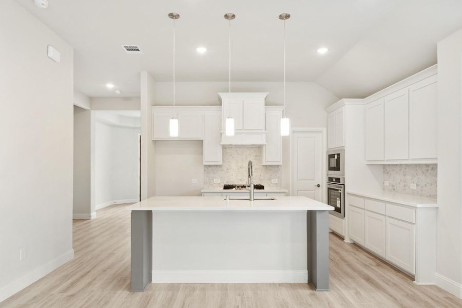 White kitchen with large center island, pendant lights, stainless steel appliances, and light wood floors