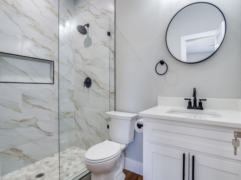 Bathroom featuring toilet, vanity, and tiled shower